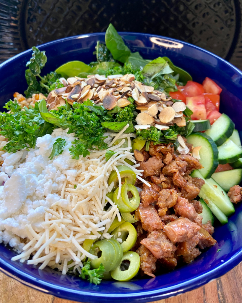 vegan antipasto couscous salad.  Made with Italian seasoning, vegan sausage, vegan cheese, olives, kale, spinach, cucumber, tomato, almonds