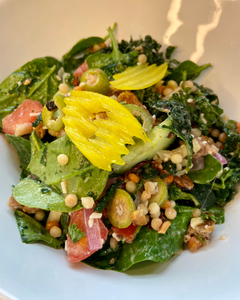 Vegan Antipasto couscous salad loaded with vegan sausage, vegan cheese, kale, spinach, cucumbers, tomatoes, onions, fennel, herbs, olives and toasted almonds.