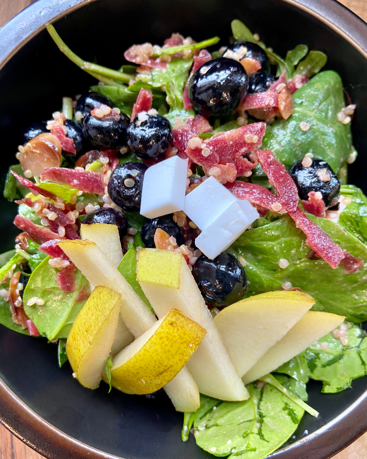 vegan Rosemary Almond Salad, made with spinach, arugula, blueberries, pear, vegan feta, quinoa, carrots, toasted almonds and a rosemary dressing.