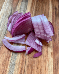 chopped red onion for Vegan Antipasto couscous salad loaded with vegan sausage, vegan cheese, kale, spinach, cucumbers, tomatoes, onions, fennel, herbs, olives and toasted almonds.