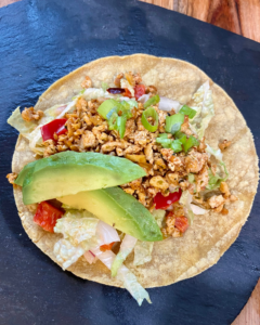 Vegan taco stuffed with spicy five spice tofu crumble, Asian red pepper slaw, fresh sliced avocado, green onion.