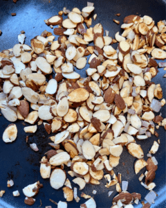 toasted almonds and shallots for Tofu and almond quinoa salad made with grapes, kale, cabbage, carrots, cucumbers, and a savory Asian dressing. 