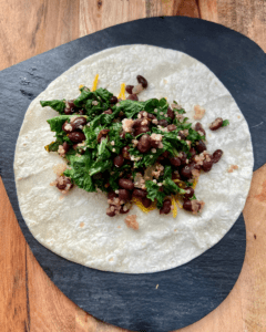 Vegan burrito, loaded with roasted sweet potatoes, toasted almonds, seasoned black beans, quinoa, kale, vegan cheese and topped with cilantro tomato salad, vegan sour cream, and avocado