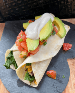 Vegan burrito, loaded with roasted sweet potatoes, toasted almonds, seasoned black beans, quinoa, kale, vegan cheese and topped with cilantro tomato salad, vegan sour cream, and avocado