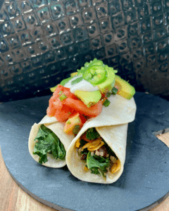 Vegan burrito, loaded with roasted sweet potatoes, toasted almonds, seasoned black beans, quinoa, kale, vegan cheese and topped with cilantro tomato salad, vegan sour cream, and avocado