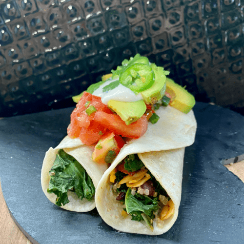 Vegan burrito, loaded with roasted sweet potatoes, toasted almonds, seasoned black beans, quinoa, kale, vegan cheese and topped with cilantro tomato salad, vegan sour cream, and avocado