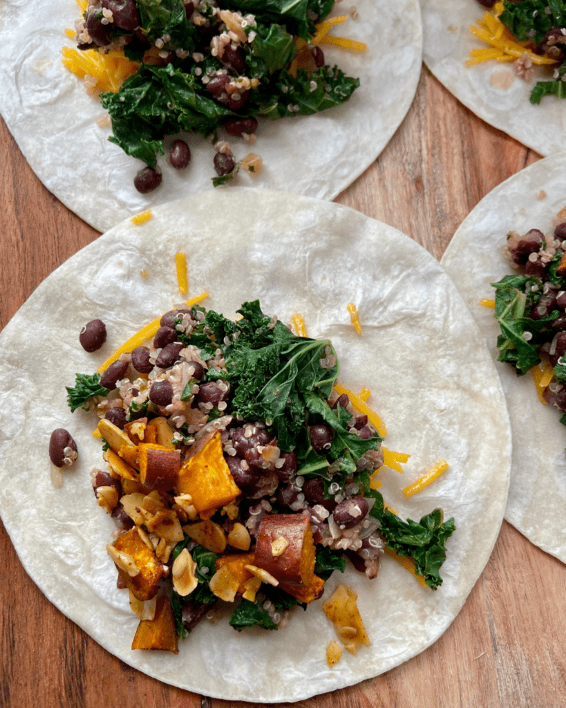 Vegan burrito, loaded with roasted sweet potatoes, toasted almonds, seasoned black beans, quinoa, kale, vegan cheese and topped with cilantro tomato salad, vegan sour cream, and avocado.