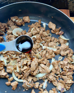 adding soy sauce to vegan steak in pan