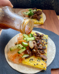 pouring sauce on the vegan steak and eggs kimchi breakfast taco