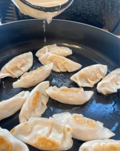 adding water to butternut squash dumplings being pan fried