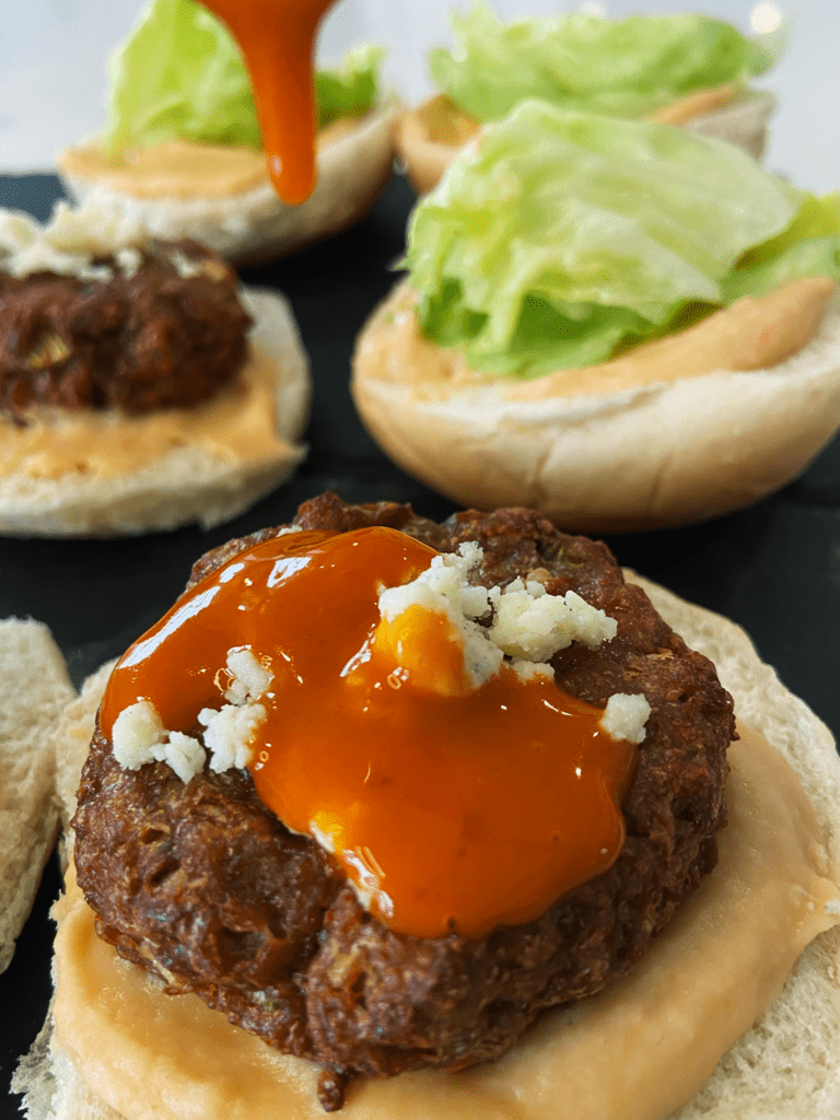 air fryer beyond meat burgers vegan buffalo blue sliders being topped with sauce